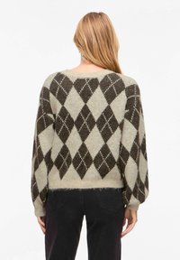 Pull en maille à coupe ample, présentant un motif en losange marron foncé et crème. Manches longues et ourlet côtelé, avec une texture douce.