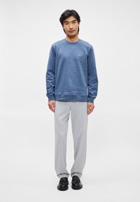 Sweatshirt azul com um acabamento texturizado e gola redonda, combinado com calças cinza claro. Os detalhes incluem um pequeno emblema no peito.