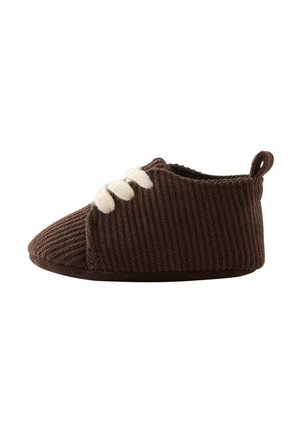 Braune Cordslipper mit einer abgerundeten Zehe, weißen Schnürsenkeln und einer Schlaufe auf der Rückseite für einfaches Anziehen. Weicher Stoff und gepolsterte Sohle.