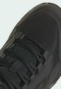 Zapatilla deportiva negra con parte superior de malla y detalles texturizados, puntera reforzada y cordones en enojos.