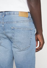 Light blue denim jeans with a classic five-pocket design. Features a brown leather label on the waistband with embossed text.