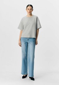 Grijze korte mouwen sweatshirt met een losse fit, gecombineerd met lichtblauwe wijde jeans en zwarte puntige hakken. Eenvoudig ontwerp met minimale accenten.