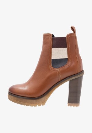 Bottine en cuir marron avec un talon bloc haut, panneaux latéraux élastiques ornés de rayures gris, crème et marine. Semelle texturée pour une meilleure adhérence.