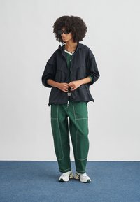 Μαύρο ελαφρύ μπουφάν με κουκούλα, πράσινο παντελόνι φόρμας με λευκές ραφές και λευκά αθλητικά παπούτσια. Τα γυαλιά ηλίου συμπληρώνουν το ντύσιμο.