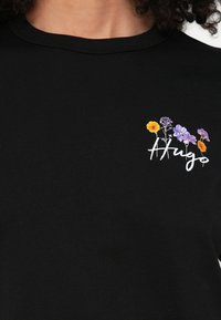 T-shirt preta de algodão com um design floral bordado em amarelo, roxo e branco. Gola redonda com mangas curtas.