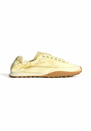 Chaussure de sport jaune clair en tissu lisse avec un design incurvé, dotée d'une semelle en caoutchouc avec de petites rondelles et des lacets.
