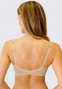 Beżowy biustonosz z regulowanymi paseczkami obszytymi koronką, teksturowanym materiałem i zapięciem na haftkę. Gładki tył z falbaniastymi brzegami.