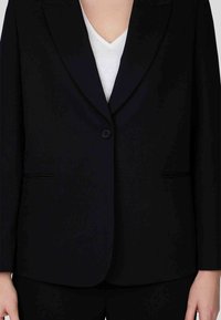 Blazer noir ajusté avec une fermeture à un bouton, des revers en pointe et deux poches avant. Fabriqué dans un tissu lisse avec une coupe structurée.
