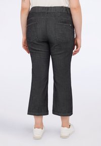 Pantaloni grigi scuri a vita alta con elastico, dotati di due tasche posteriori e una texture denim liscia. Indossati con sneakers bianche.