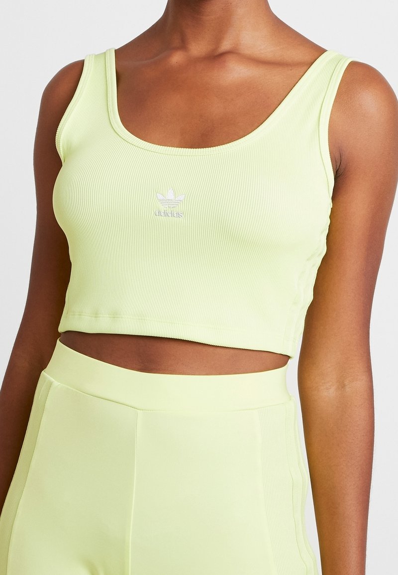 Jasnozielony prążkowany top crop z szerokimi ramiączkami, z małym białym logo na klatce piersiowej. Materiał ma gładką teksturę, dopasowany krój.