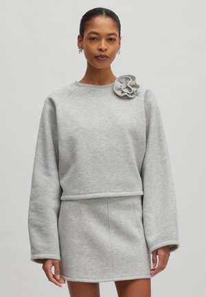 Gray sweatshirt with a round neckline and long sleeves, featuring a textured floral accent on the left shoulder and a fitted waistband.