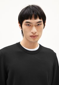 Schwarzer Pullover mit geripptem Rundhalsausschnitt, gefertigt aus einem glatten, strukturierten Stoff. Das Design ist minimalistisch, ohne sichtbare Muster oder Akzente.