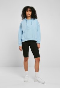 Világoskék, oversized kapucnis felső, elülső zsebbel és húzózsinórral, fekete biker shortsszal és fehér, texturált talpú sportcipőkkel párosítva.