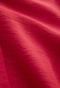 Tissu rouge avec une texture fine visible et des plis souples créant des variations de lumière et d'ombre sur la surface.