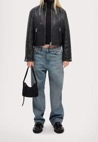 Veste courte en cuir noir avec fermetures éclair argentées, pull en laine bleu marine, jean large bleu clair, sac à main noir et chaussures noires brillantes.