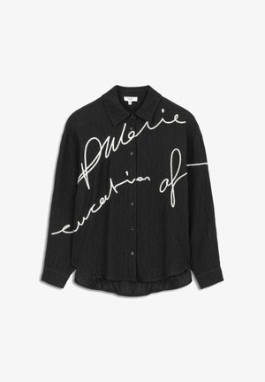 Chemise noire à boutons avec un tissu texturé. Présente une broderie en style manuscrit blanche sur le devant, un ourlet allongé et des manches à revers.