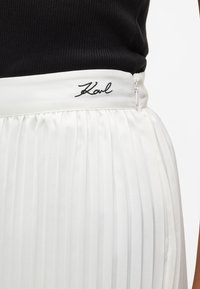 Biała plisowana spódnica z gładkim pasem; wyróżnia się czarnym haftem "Karl"; wykonana z lekkiego materiału, zaprojektowana z myślą o zwiewnej sylwetce.