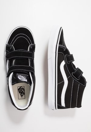 Paire de baskets Vans noir et blanc avec des brides Velcro, couture blanche et une bande latérale blanche, vues de dessus et de côté.