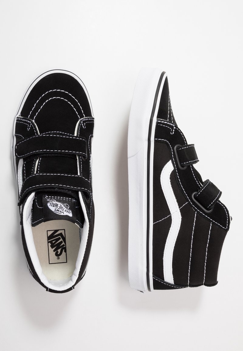 Paire de baskets Vans noir et blanc avec des brides Velcro, couture blanche et une bande latérale blanche, vues de dessus et de côté.