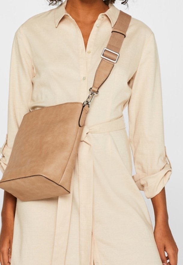 Tan crossbody-taske med en struktureret form, glat kunstlædermateriale og en kontrasterende sort kant. Justerbar rem med metalbeslag.