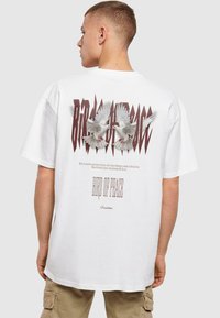 White oversized t-shirt featuring a graphic design of two doves and text on the back, with a loose fit and rolled sleeves.