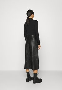 Svart långärmad topp som matchas med höga svarta läder culottes, med en slät yta och vida ben. Svarta snörboots fulländar looken.