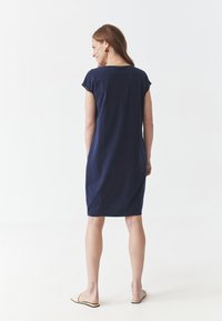 Robe en coton bleu marine à manches courtes, à coupe décontractée et fentes sur les côtés, avec un col rond et une longueur intermédiaire.