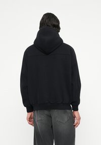 Sweat à capuche noir avec une coupe décontractée, des poignets et une taille côtelés. Texture lisse, sans motifs ni logos visibles.