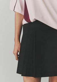 Jupe plissée noire avec une finition texturée, associée à un haut rose avec des accents bordeaux et une coupe décontractée.