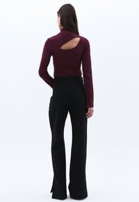Bordeaux långärmad topp med en back cutout, kombinerad med svarta utsvängda byxor. Slät tygkvalitet med en åtsittande design.
