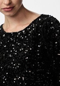 Top nero con paillettes, dalla scollatura rotonda, caratterizzato da paillettes dense e lucenti che creano una superficie texturizzata. Il tessuto appare morbido e soffice.