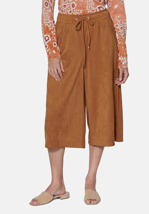 Pantalons culottes marron en tissu ressemblant à du daim, dotés d'une taille élastique avec un cordon de serrage. Associés à des sandales ouvertes beiges.