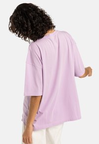 Tricou lila, din bumbac, cu croială lejeră, maneci scurte și decolteu rotund. Spatele are o textură netedă și fără modele vizibile.