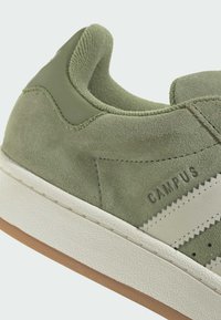 Zelené semišové tenisky s bielym, cik-cak pruhom a textúrovanou gumovou podrážkou. Obsahujú polstrovaný golier a embosované logo značky.