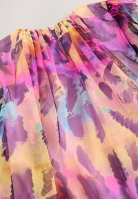 Robe légère et transparente avec des motifs floraux multicolores en rose, violet et jaune, dotée d'un encolure froncée et d'une fermeture boutonnée à l'arrière.