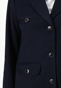 Blazer navy en tissu texturé, à double boutonnage, avec deux poches avant à rabat et boutons argentés.