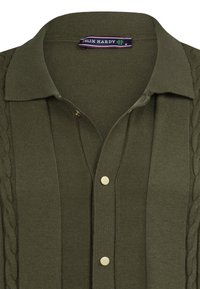 Olivengrøn strikket polo shirt med ribbet tekstur, kabelstrikdetaljer på siderne og guldbelagte knapper ved halsudskæringen.