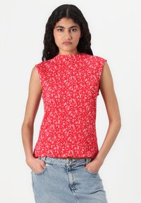Rød ermeløs topp med plissert design, som har et lite blomstermønster i hvitt. Stoffet synes lett og teksturert.