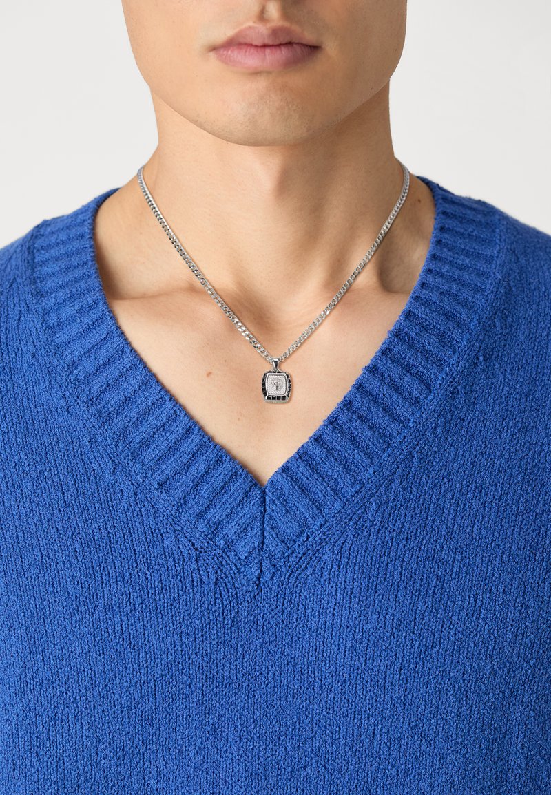 Maglione a V in maglia blu brillante e testurizzata. Collana in argento con un ciondolo quadrato che pende dal collo. Finitura liscia e dettagliata.