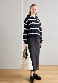 Felpa a righe navy con righe bianche, abbinata a una gonna di jeans scuri. Tiene in mano una borsa color crema e indossa mocassini neri.