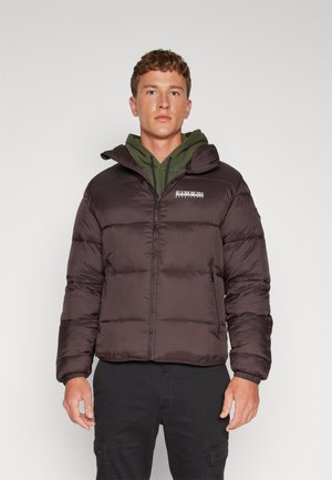 Dunkelbraune Steppjacke mit Kapuze, Reißverschluss, gestepptem Muster und Logodetail. Über einem grünen Hoodie getragen, kombiniert mit schwarzen Hosen.