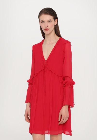 Robe rouge fluide en tissu léger, présentant un décolleté en V profond, des accents froncés et de longues manches avec des détails noués aux poignets.