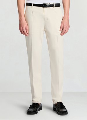 Pantaloni beige da donna con taglio dritto, fronte piatto, due pieghe e cintura in pelle nera. Indossati con mocassini neri. Tessuto liscio.