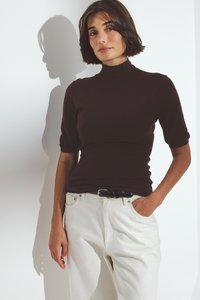 Lyhythihainen, poolokauluspaita tummanruskeasta puuvillasta, yhdistettynä korkeavyötäröisiin valkoisiin farkkuihin. Mukana musta vyö, sileä rakenne ja kevyesti joustava materiaali.