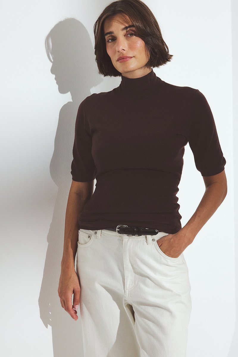 Lyhythihainen, poolokauluspaita tummanruskeasta puuvillasta, yhdistettynä korkeavyötäröisiin valkoisiin farkkuihin. Mukana musta vyö, sileä rakenne ja kevyesti joustava materiaali.