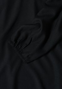 Schwarzer Stoff mit einer glatten Textur, der eine geraffte Manschettendetail aufweist. Das Gesamtbild ist einheitlich und gleichmäßig, ohne zusätzliche Muster.