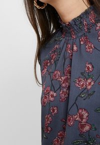 Námořnická květinová blůza s volantovým výstřihem, jemnou růžovou a zelenou výšivkou a splývavým materiálem s měkkou strukturou.