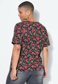 Czarny t-shirt w kwiatowy wzór z czerwonymi różami i zielonymi liśćmi. Krótkie rękawy, luźny krój, z okrągłym dekoltem. Dopełnieniem stroju są szare jeansy.