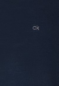 Marint textil med präglad "ck"-logotyp; slät yta, subtilt mönster, inga synliga detaljer eller utsmyckningar.