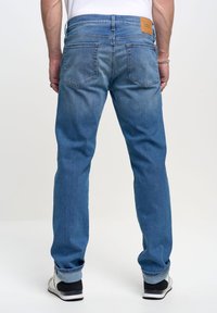 Jeans de denim azul con corte recto, que cuentan con cinco bolsillos y un lavado claro. La cinturilla tiene un parche de cuero y el dobladillo está remangado.